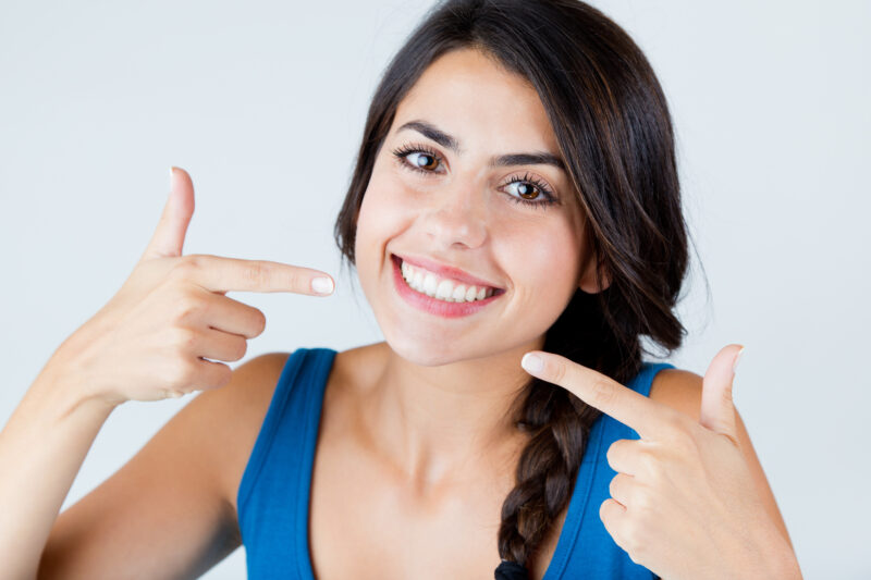 Smiling woman pointing at her bright white teeth after cosmetic dentistry treatment at Dominion Smiles in San Antonio, TX